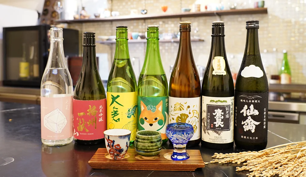 Seven Japanese sake bottles with traditional cups on a wooden tray